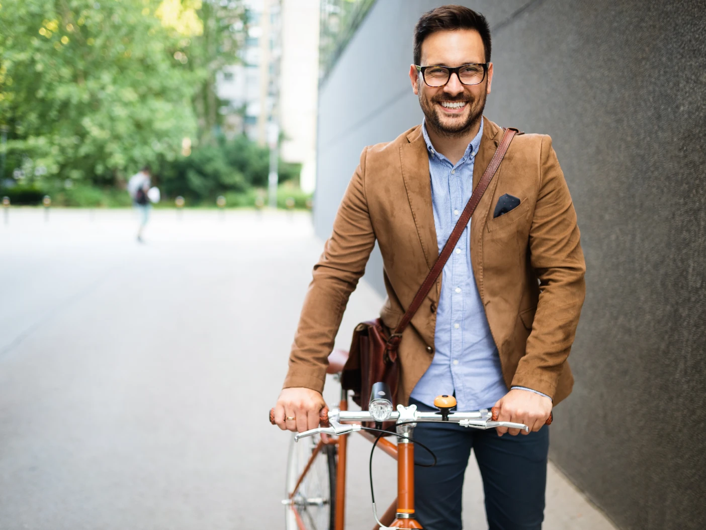 A professional man smiles while holding his bicycle in an urban setting
